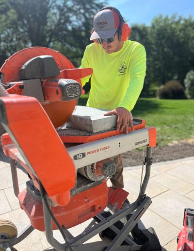 Worker operating a stone saw for patio installation by Weadickbros Landscape Design & Build